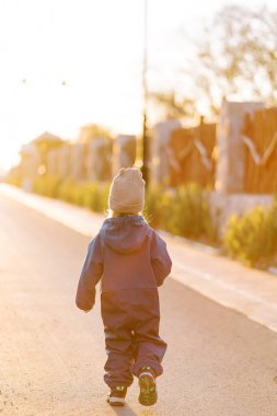 Küçük kız, oyulmuş ahşap bir çit boyunca güneşli bir yolda yürüyor. Arkadan bak. Yüksek kalite fotoğraf