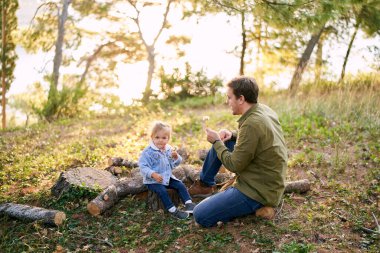 Baba ve küçük kız ellerinde karahindiba ile kütüklerin üzerinde oturuyorlar. Yüksek kalite fotoğraf