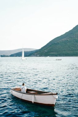 Balıkçı beyaz bir balıkçı teknesinde oturur ve denize bakar. Arkadan bak. Yüksek kalite fotoğraf