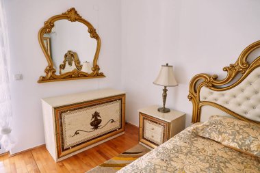 Göğsünün üstündeki duvarda, çekmeceleri ve çift kişilik yatağı olan oyulmuş bir çerçevede ayna. Yüksek kalite fotoğraf