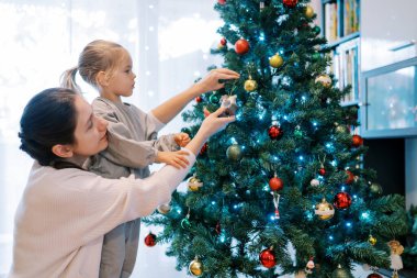Küçük kız, Noel ağacına oyuncak asarken annesinin dizlerinin üzerinde duruyor. Yüksek kalite fotoğraf