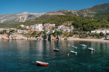 Boats are moored in the sea off a mountainous coast lined with colorful hotels. Przno, Montenegro. High quality photo clipart