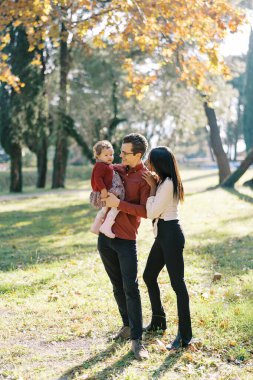 Annem, babasının yanında kollarında küçük bir kız çocuğuyla ellerini omuzlarına koyuyor. Yüksek kalite fotoğraf