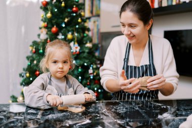 Merdaneli küçük kıza bakarken gülümseyen anne hamur yoğuruyor. Yüksek kalite fotoğraf