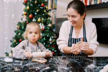Dili sarkık küçük bir kıza bakarken hamuru yoğuran gülen anne. Yüksek kalite fotoğraf