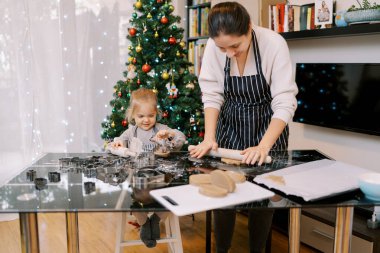 Masada annesinin yanında oturan gülümseyen küçük kız zencefilli ekmek hamuru yapıyor. Yüksek kalite fotoğraf