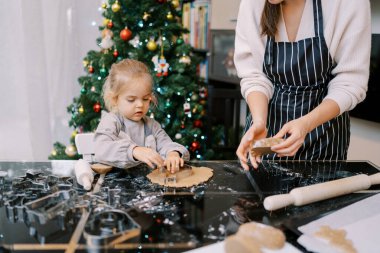 Küçük kız hamurun üzerine hamuru yoğuran annesinin yanına kurabiye keskisi koyar. Yüksek kalite fotoğraf
