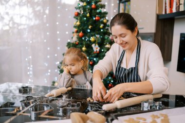 Küçük kız annesinin yanında eli üzerinde dinlenerek masada oturur ve kesilmiş kurabiyeleri katlar. Yüksek kalite fotoğraf
