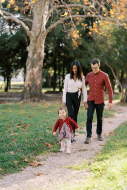 Annem ve babam bir sonbahar parkında küçük bir kızı takip ederken sarılıyorlar. Yüksek kalite fotoğraf