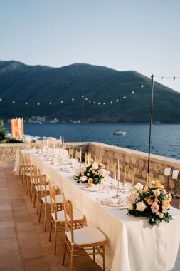 Mumlar ve çiçek buketleriyle dolu bir şölen masası deniz kenarında bir terasta duruyor. Yüksek kalite fotoğraf