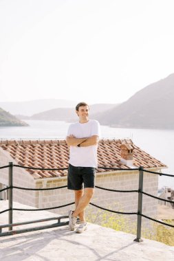 Gülümseyen bir adam, kollarını kavuşturarak, bir gözlem güvertesinde bir halat teline yaslanır. Perast, Karadağ. Yüksek kalite fotoğraf