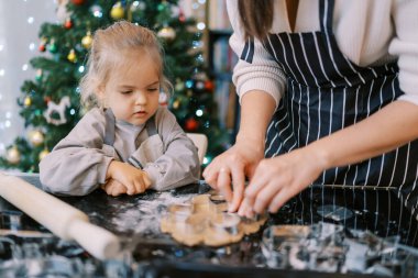 Küçük kız, annesine, masada metal kurabiye keskisiyle hamuru keserken bakıyor. Kırpılmış. Yüksek kalite fotoğraf
