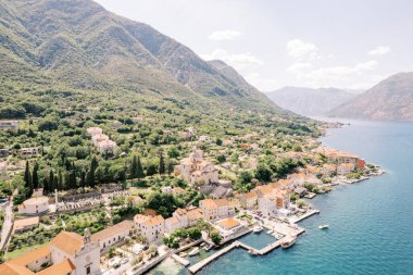 Yeşil dağların eteğindeki bir tepede kilisesi olan antik bir kasabanın kıyısındaki iskelede. Prcanj, Karadağ. Drone. Yüksek kalite fotoğraf