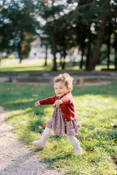 Küçük gülümseyen kız yeşil çimenlerde kolları açık yürüyor. Yüksek kalite fotoğraf