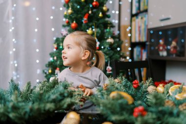 Masada elinde Noel çelengiyle oturan ve yüzünü çeviren küçük bir kız. Yüksek kalite fotoğraf
