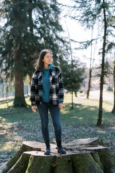 Kız yosunla kaplı kocaman bir kütüğün üzerinde duruyor ve başka tarafa bakıyor. Yüksek kalite fotoğraf