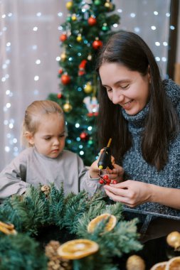 Küçük kız, annesinin yılbaşı çelengi için silahından çıkan böğürtlenleri yapıştırmasına yardım ediyor. Yüksek kalite fotoğraf