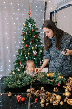 Küçük kız elinde tutkal tabancasıyla annesine yılbaşı çelengi olarak meşe palamudu veriyor. Yüksek kalite fotoğraf