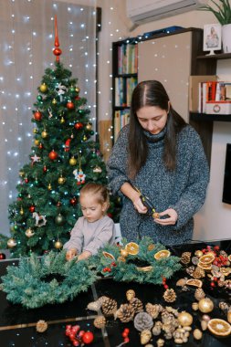 Küçük kız çam kozalaklarını Noel çelengine yapıştırıyor. Annesi de tabancayla yapıştırıyor. Yüksek kalite fotoğraf