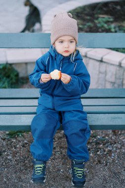 Küçük kız, elinde ısırılmış bir elmayla parkta bir bankta oturuyor. Yüksek kalite fotoğraf