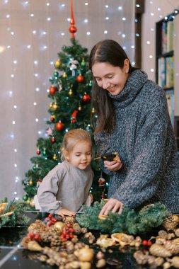 Küçük kız gülümseyen annesine bakar ve bir parça kuru portakalı masaya yapıştırır. Yüksek kalite fotoğraf