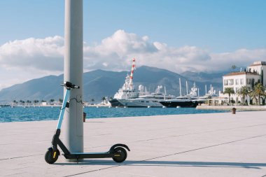 Kiralık elektrikli scooter, deniz kıyısında demirli yatları olan bir rıhtımın yanında duruyor. Yüksek kalite fotoğraf