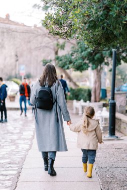 Anne ve küçük bir kız kaldırım taşı caddesinde el ele yürüyorlar. Arkadan bak. Yüksek kalite fotoğraf