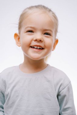 Gri arka planda başını yana eğen gülen küçük bir kızın portresi. Yüksek kalite fotoğraf