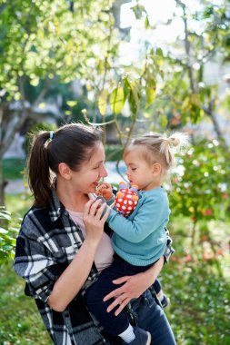 Gülümseyen anne, elinde oyuncaklarla bahçede otururken küçük kıza bakıyor. Yüksek kalite fotoğraf