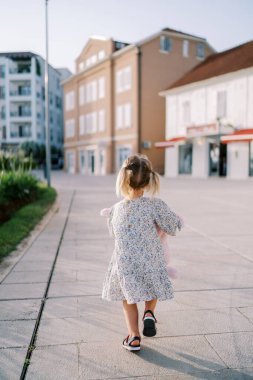 Pembe oyuncak tavşanlı küçük bir kız apartmana giden yolda yürüyor. Arkadan bak. Yüksek kalite fotoğraf