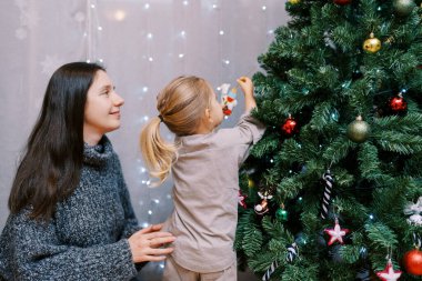 Annem, bir yılbaşı ağacına lama heykelciği asan küçük bir kıza bakıyor. Yüksek kalite fotoğraf