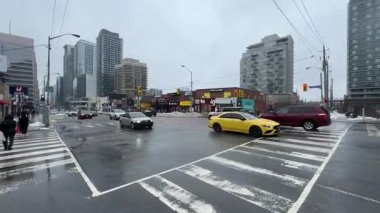 Araç ve yayalarla dolu yoğun bir şehir kavşağı, yağan yağmurla canlanıyor.