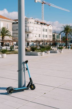 Kiralık elektrikli scooter, gezinti güvertesindeki direğe bağlı duruyor. Yüksek kalite fotoğraf
