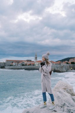 Genç bir kadın eski Budva kasabasının arka planına karşı montuyla kayalık bir sahilde duruyor. Karadağ. Yüksek kalite fotoğraf