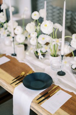 Menü, beyaz çiçeklerle dolu bir şenlik masasındaki peçetenin üzerinde duran siyah bir tabağın yanında duruyor. Yüksek kalite fotoğraf