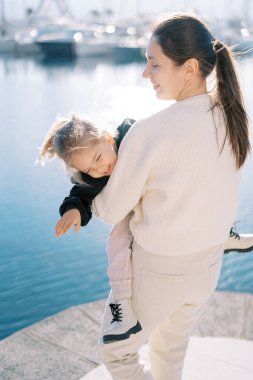 Gülümseyen anne, iskelede dururken küçük gülen kızı kollarıyla çeviriyor. Arkadan bak. Yüksek kalite fotoğraf