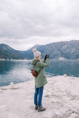Turist rıhtımda duruyor ve akıllı bir telefonla dağların fotoğraflarını çekiyor. Yan görüş. Yüksek kalite fotoğraf