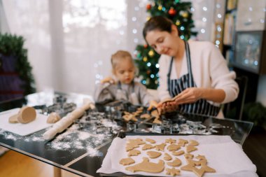 İçinde zencefilli kurabiye olan bir çarşaf bir anne ve hamuru inceleyen küçük bir kızın yanında duruyor. Yüksek kalite fotoğraf