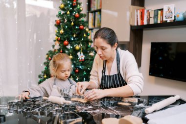 Annem küçük bir kıza zencefilli ekmek hamuruna nasıl kurabiye keskisi konulacağını gösteriyor. Yüksek kalite fotoğraf