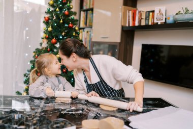 Gülümseyen anne, masada zencefilli ekmek hamuru yuvarlarken küçük kızla burun buruna dokunuyor. Yüksek kalite fotoğraf