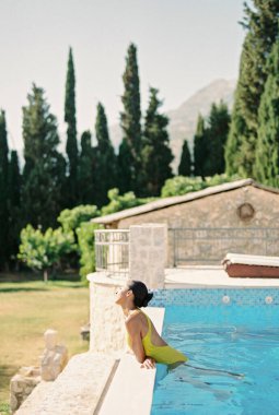 Genç bir kadın havuzda dikilirken, dirseklerini yana doğru eğerek güneşleniyor. Yan görüş. Yüksek kalite fotoğraf