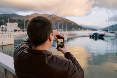 Adam gün batımında yat ile marinayı akıllı telefonuyla vuruyor. Arkadan bak. Yüksek kalite fotoğraf