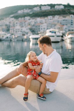 Küçük gülen kız babasının kucağında oturmuş kaldırımda ona bakıyor. Yüksek kalite fotoğraf