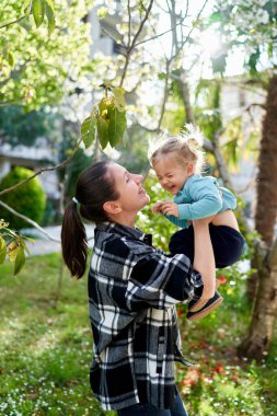 Annem yeşil bir bahçede kollarında gülen bir kız yakalıyor. Yüksek kalite fotoğraf