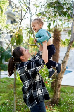 Gülümseyen anne bahçede dururken kollarında gülen küçük kızı kaldırır. Yüksek kalite fotoğraf