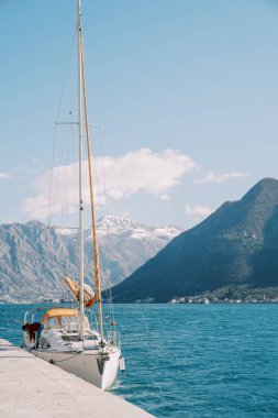 Küçük beyaz yelkenli yatı, bir rıhtıma demirlemiş dağların arkasına karşı. Yüksek kalite fotoğraf
