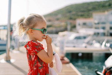 Küçük kız elinde oyuncak bir tavşanla iskelede dururken simit yiyor. Yan görüş. Yüksek kalite fotoğraf