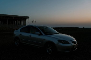 Araba alacakaranlıkta binanın yanındaki deniz kıyısında duruyor. Yüksek kalite fotoğraf