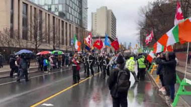 Renkli bir geçit töreninde yağmurlu bir sokakta bayrak ve coşkulu yürüyüşçüler sergileniyor