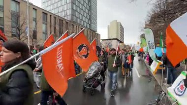 Büyük bir kalabalık canlı bir geçit töreninde bulutlu gökyüzünün altında renkli bayraklarla yürüyor.